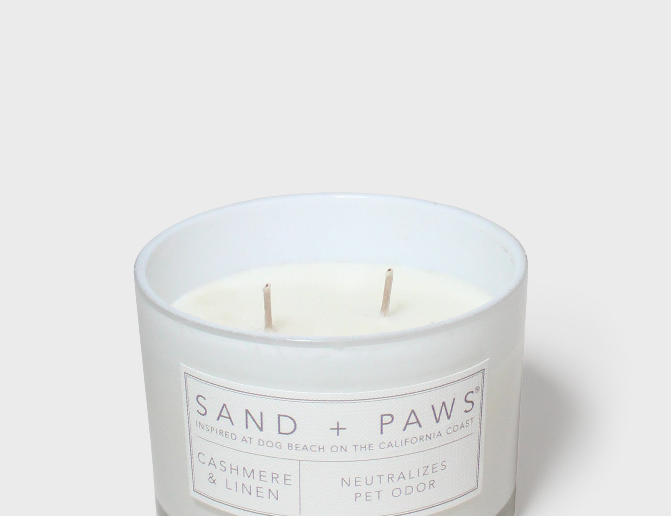 Scented candle in white glass jar with Sand + Paws label and two wicks
