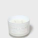 White scented candle jar with 'SAND + PAWS' label and two wicks
