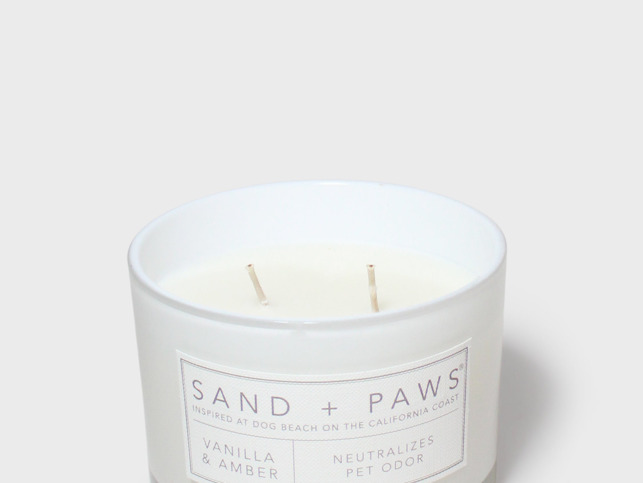 White scented candle jar with 'SAND + PAWS' label and two wicks