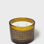 Gold-rim candle jar with white wax and two wicks, labeled Vanilla Sandalwood