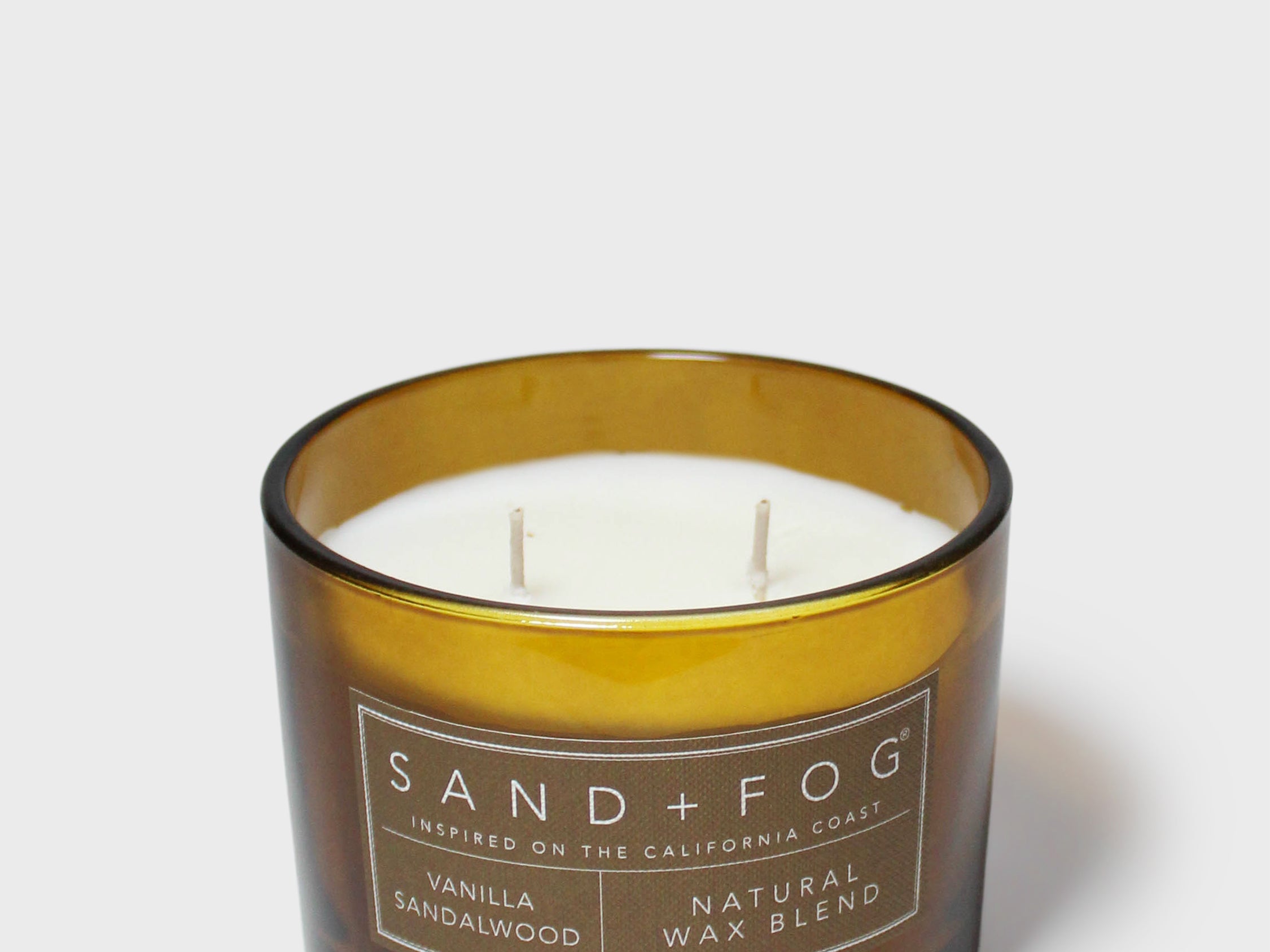 Gold-rim candle jar with white wax and two wicks, labeled Vanilla Sandalwood