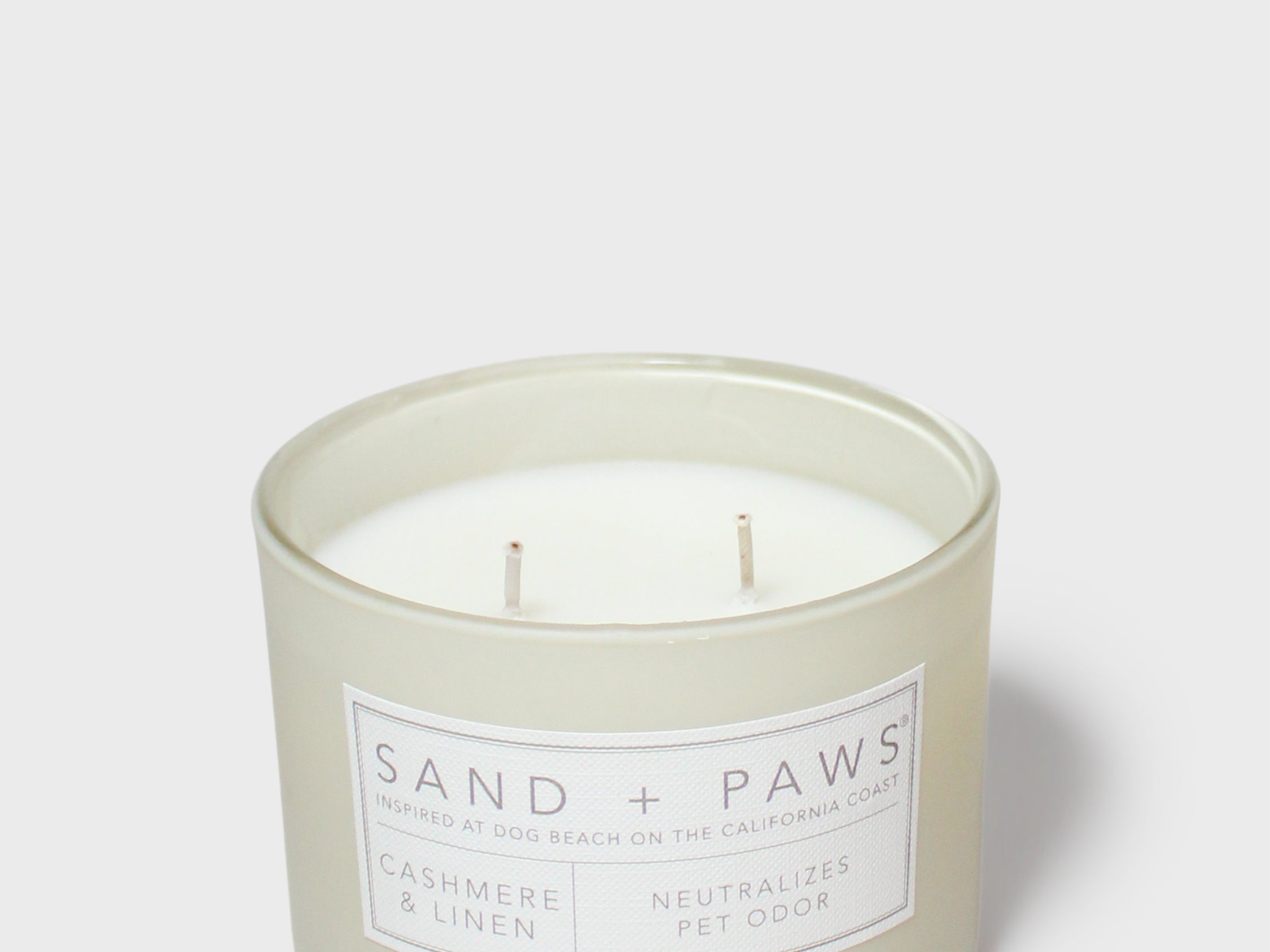 Mint green scented candle in jar with “SAND + PAWS” label and two wicks