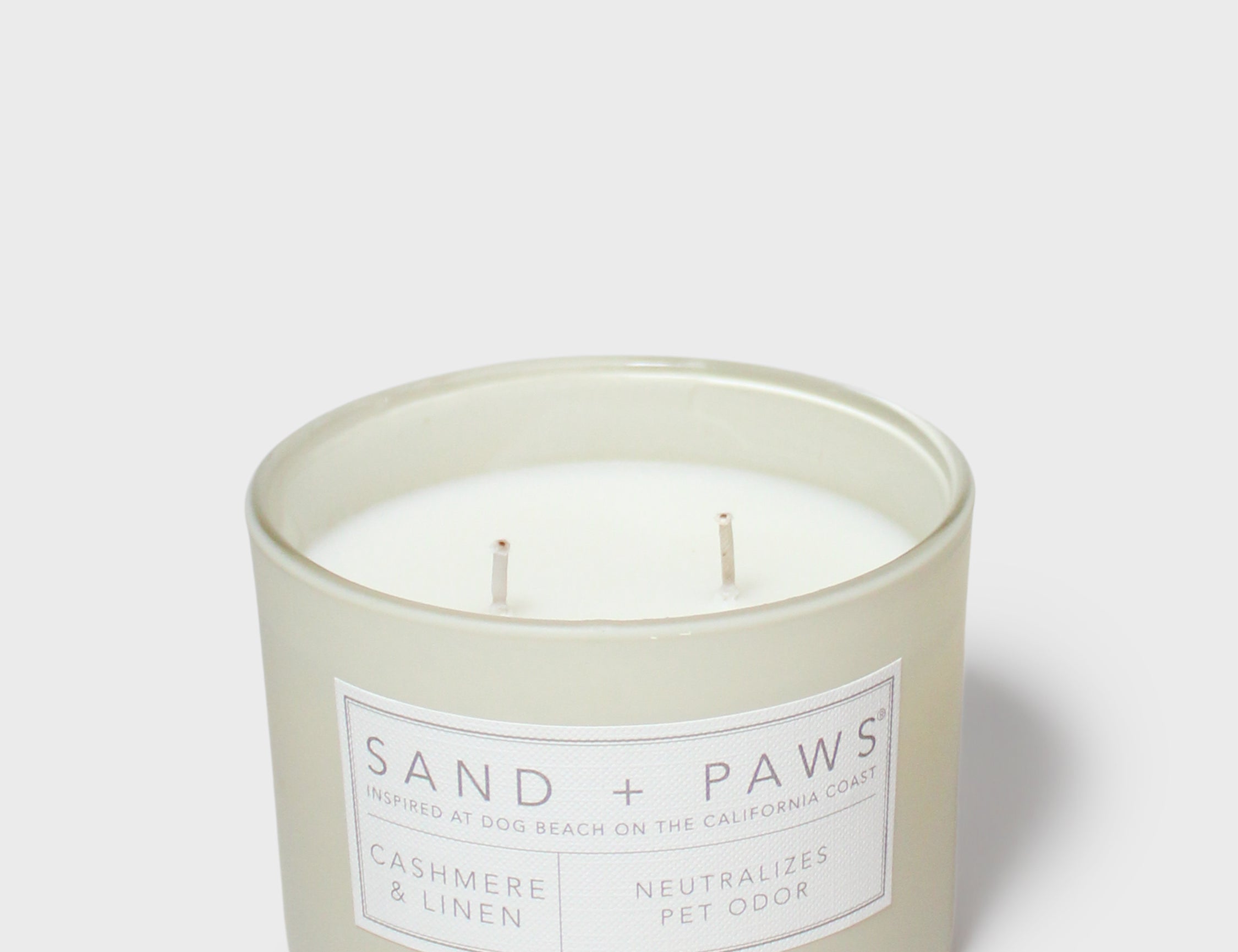 Mint green scented candle in jar with “SAND + PAWS” label and two wicks