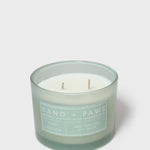 Scented candle in teal glass jar with white label and two visible wicks