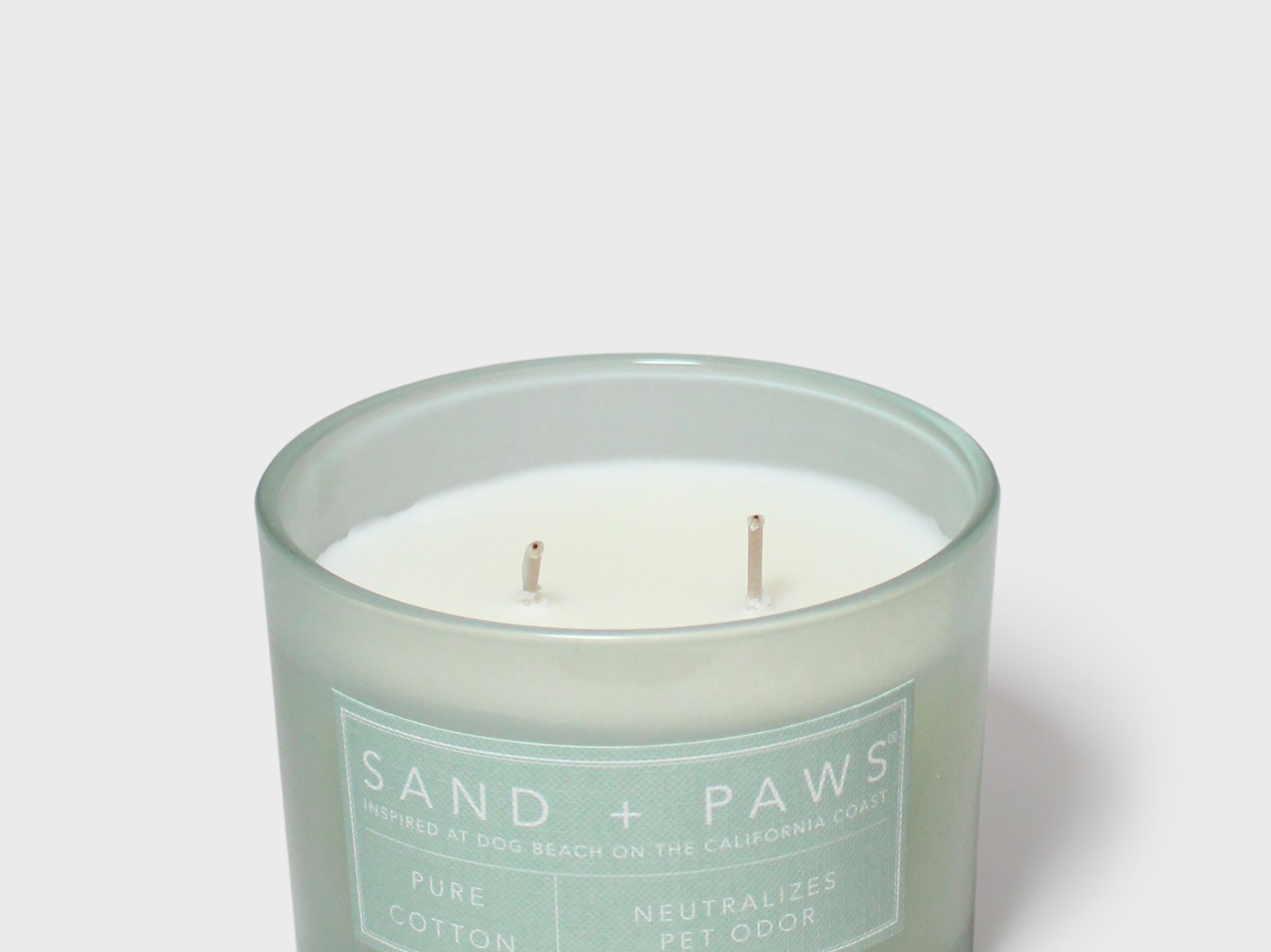 Scented candle in teal glass jar with white label and two visible wicks