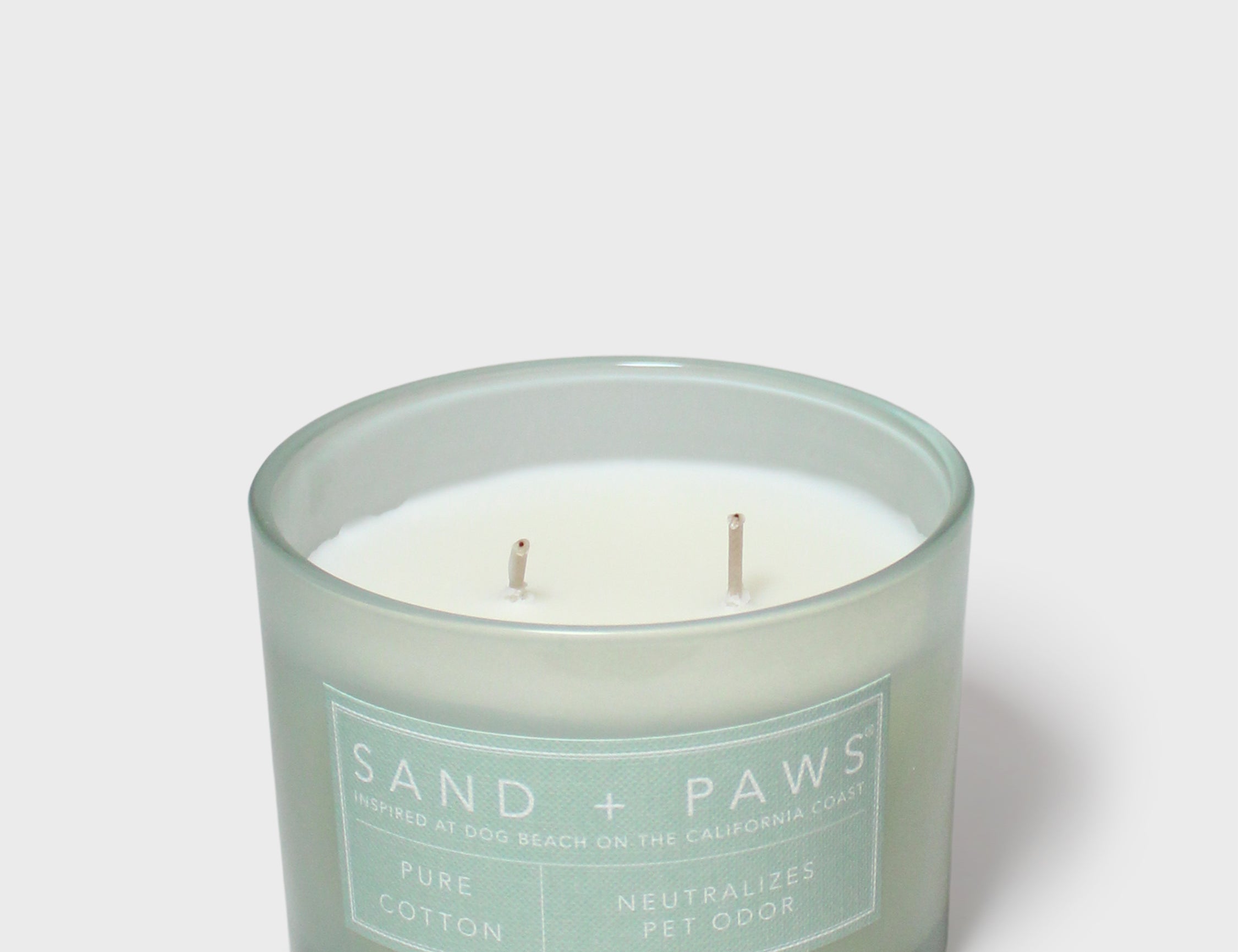 Scented candle in teal glass jar with white label and two visible wicks