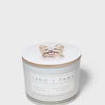 White scented candle with dog portrait lid and Sand + Paws label on jar