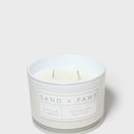 White glass scented candle jar with two wicks and Sand + Paws label