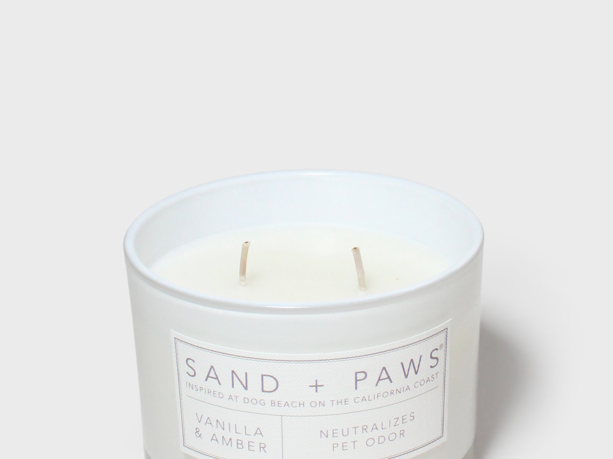 White glass scented candle jar with two wicks and Sand + Paws label