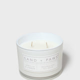 White glass scented candle jar with two wicks and Sand + Paws label