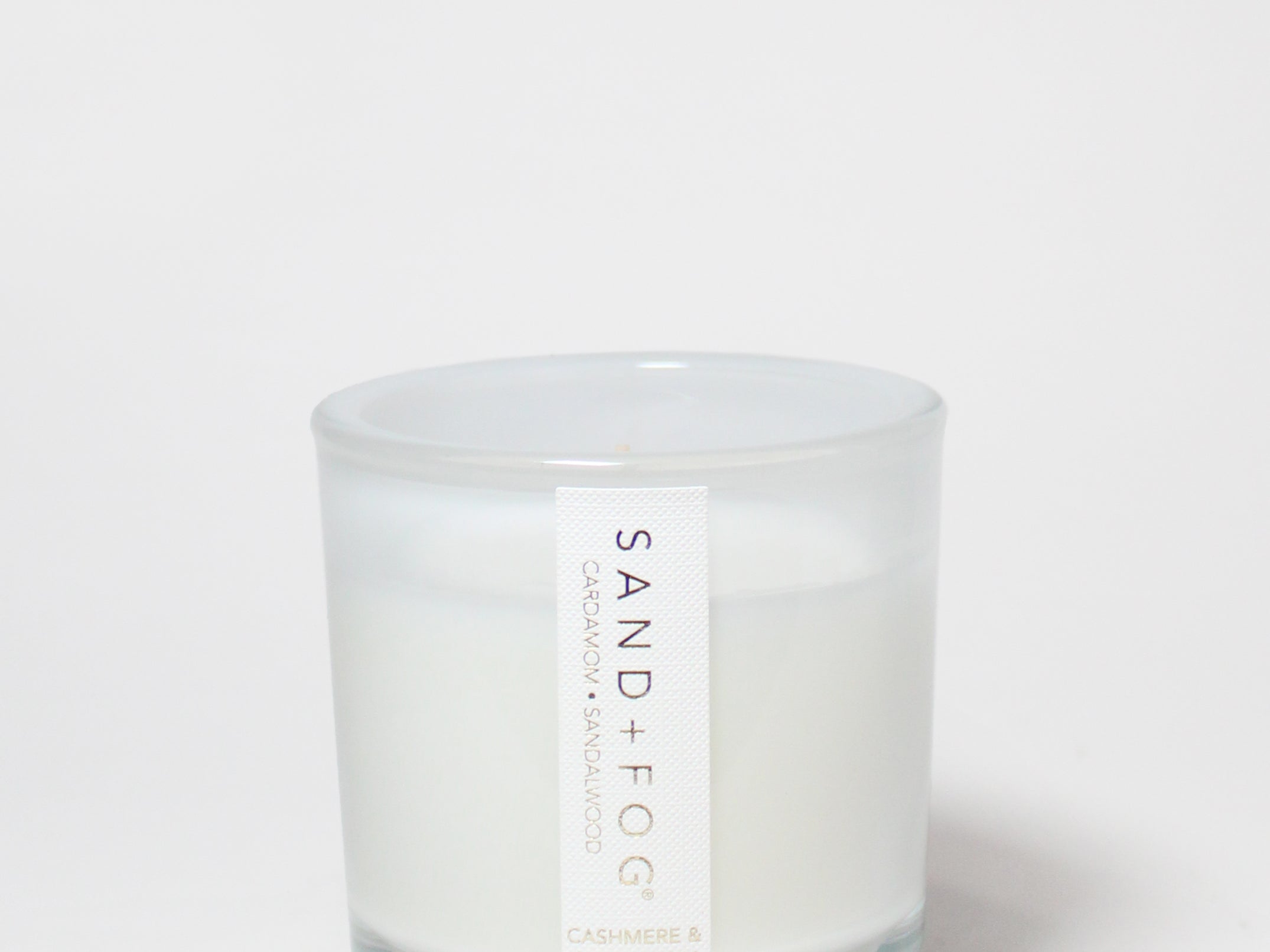 Cashmere & Cardamom scented candle in a clear glass jar with a white wax fill and label.