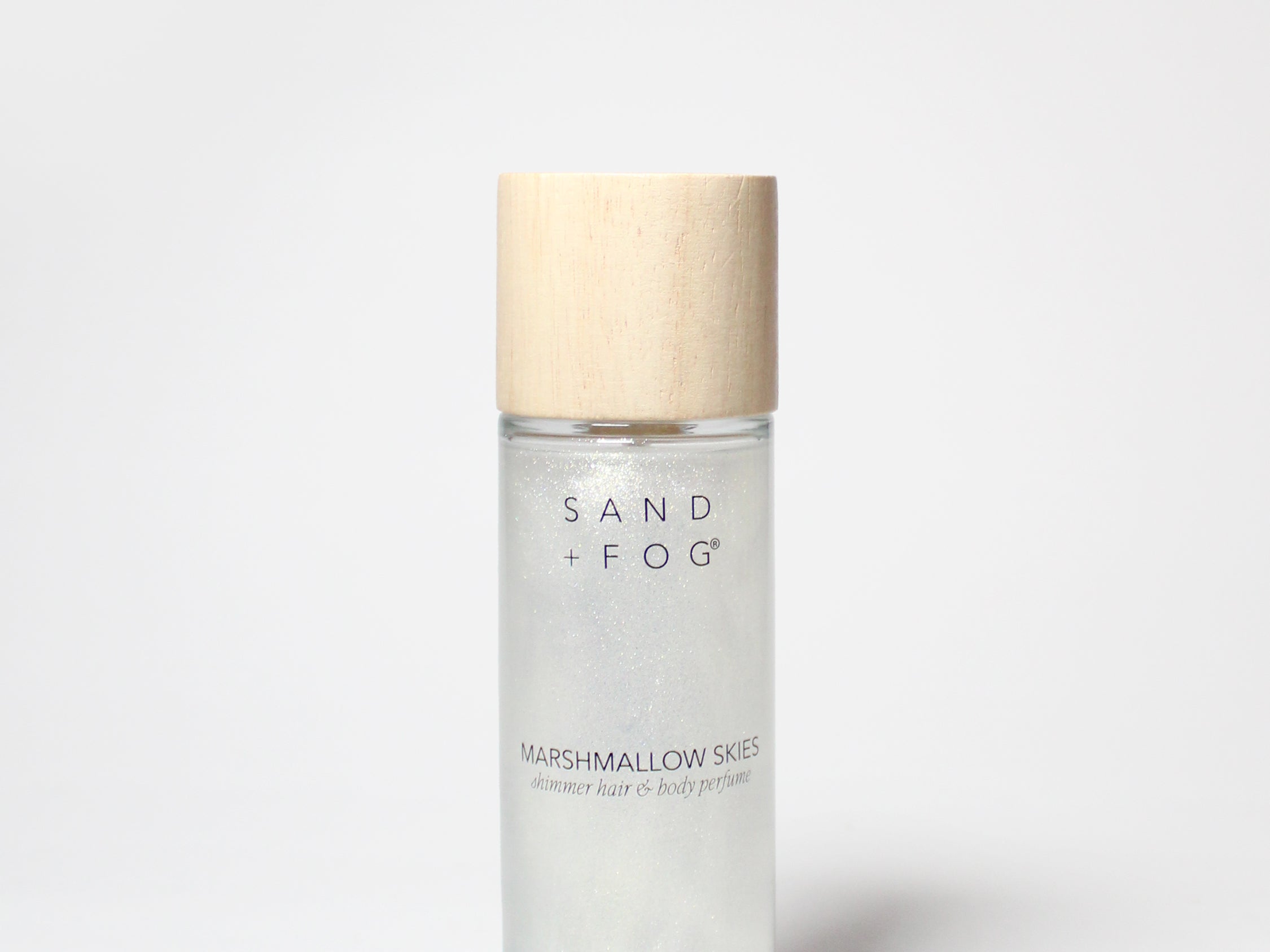 Hair and body perfume bottle with wood-toned cap, clear bottle, Sand + Fog label.