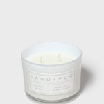 Scented candle jar with Sand + Fog label and cream wax