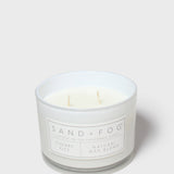 Scented candle jar with Sand + Fog label and cream wax
