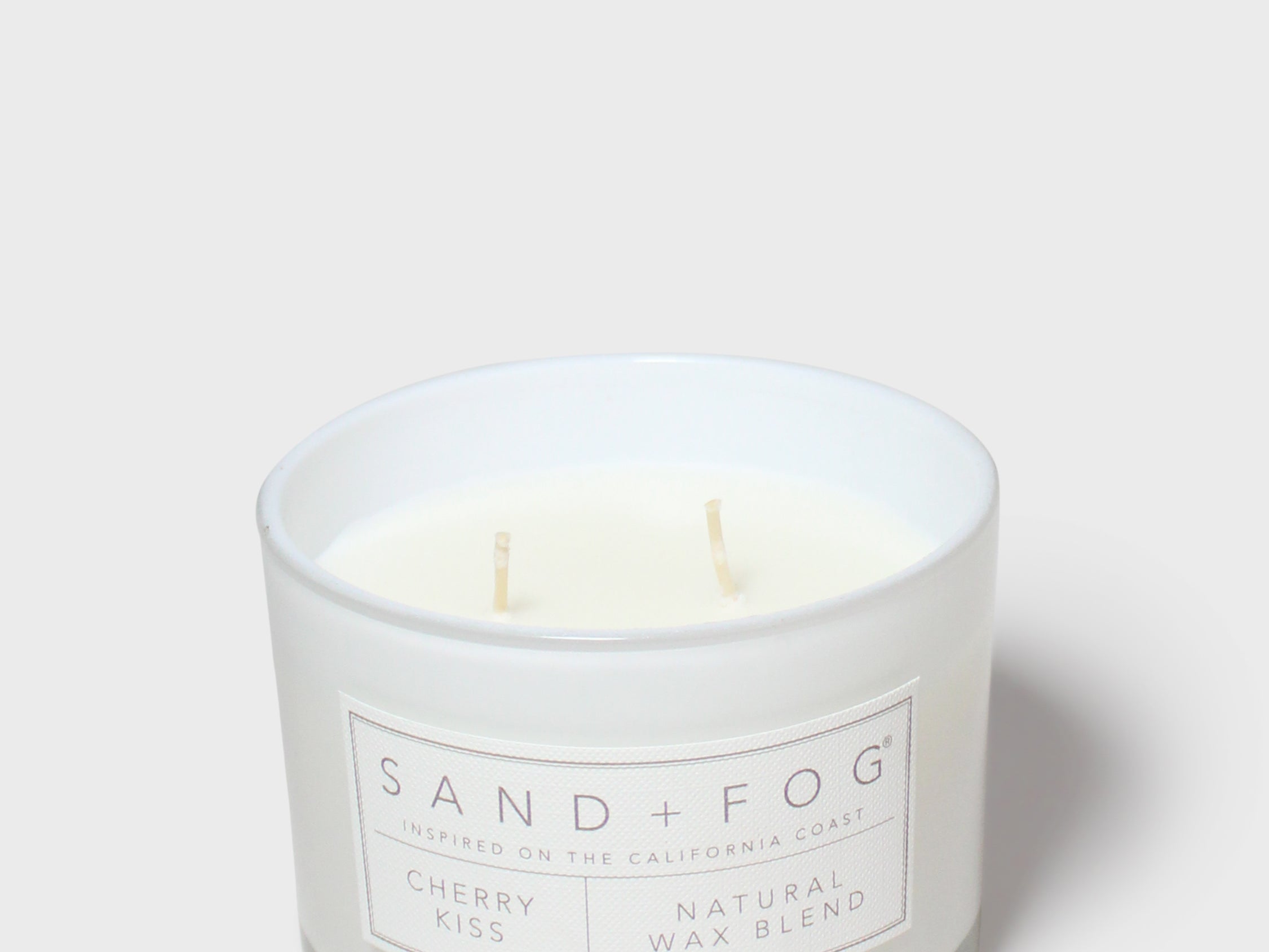 Scented candle jar with Sand + Fog label and cream wax