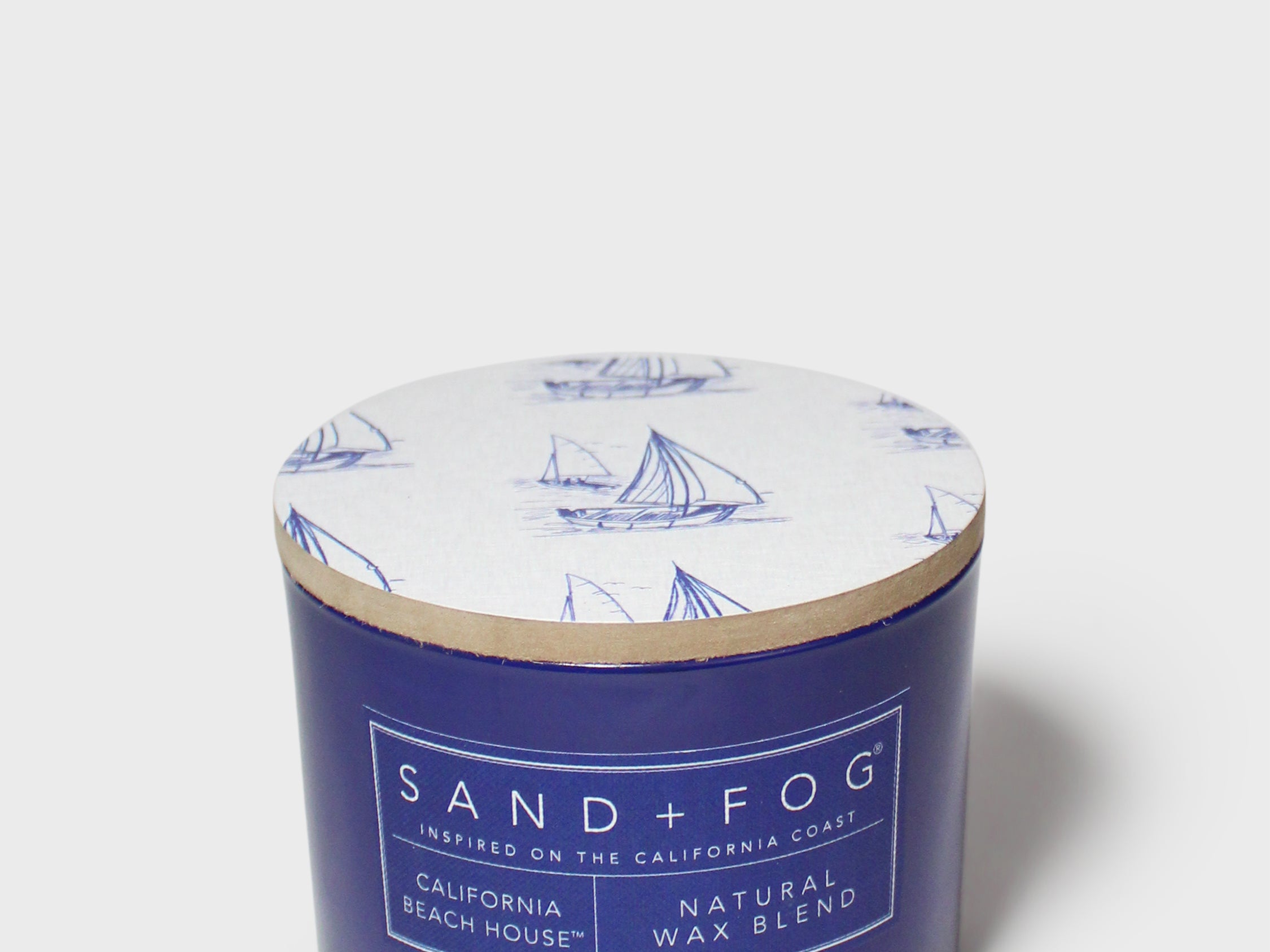 Blue scented candle jar with sailboat lid and SAND+FOG California Beach House label