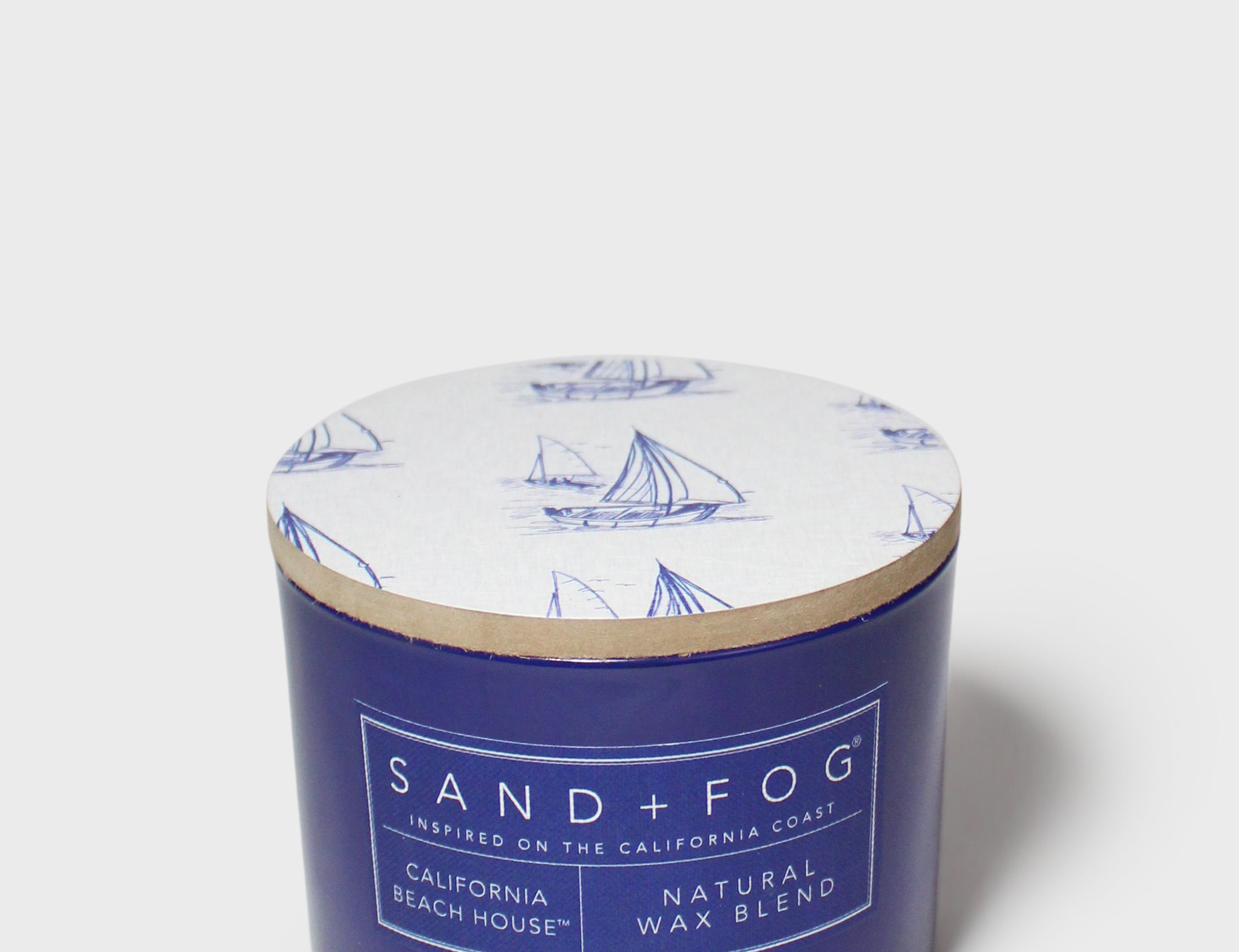 Blue scented candle jar with sailboat lid and SAND+FOG California Beach House label