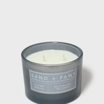 Dark gray scented candle jar with 'Sand + Paws' label and two white wicks