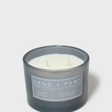 Dark gray scented candle jar with 'Sand + Paws' label and two white wicks