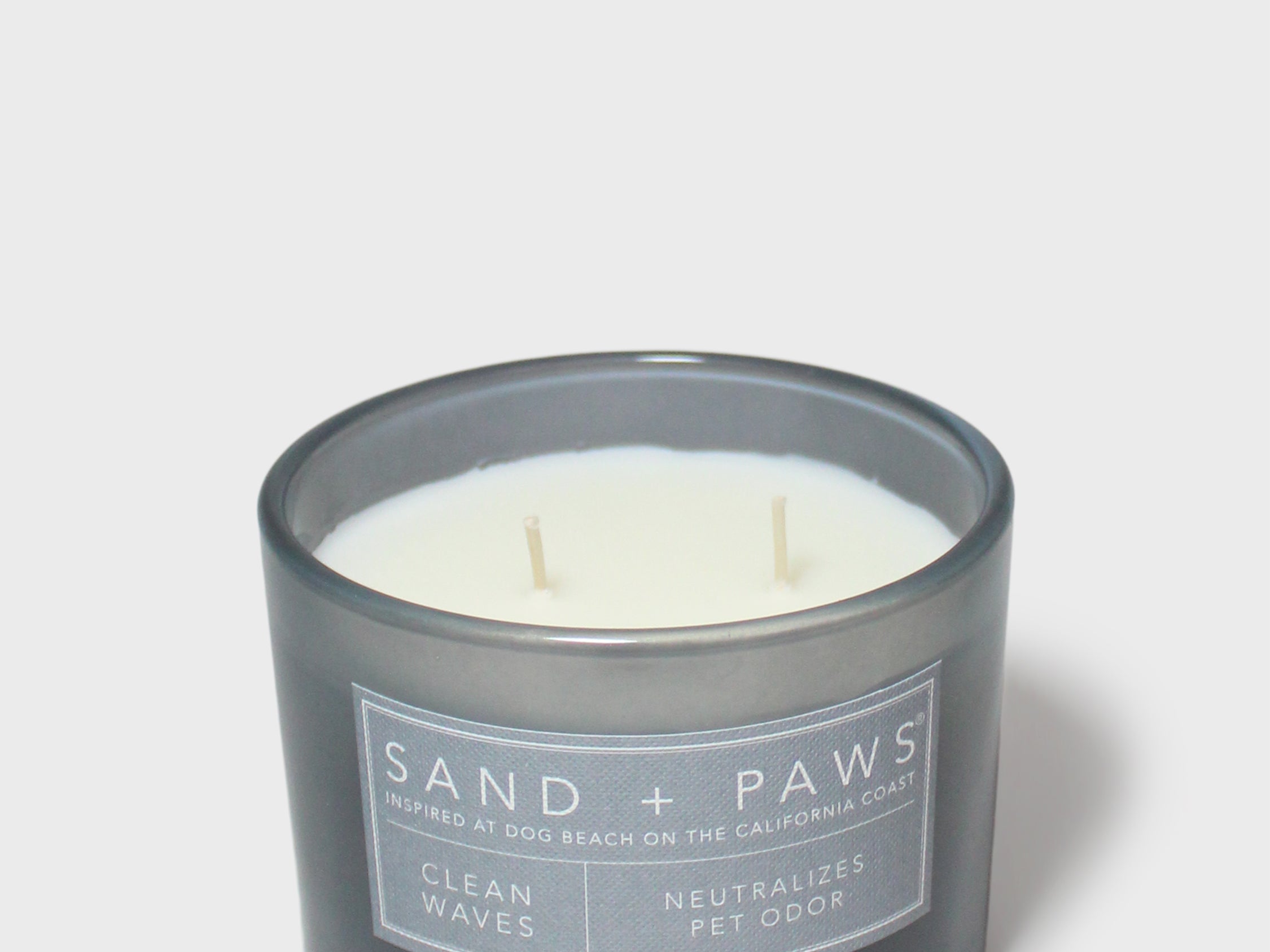 Dark gray scented candle jar with 'Sand + Paws' label and two white wicks