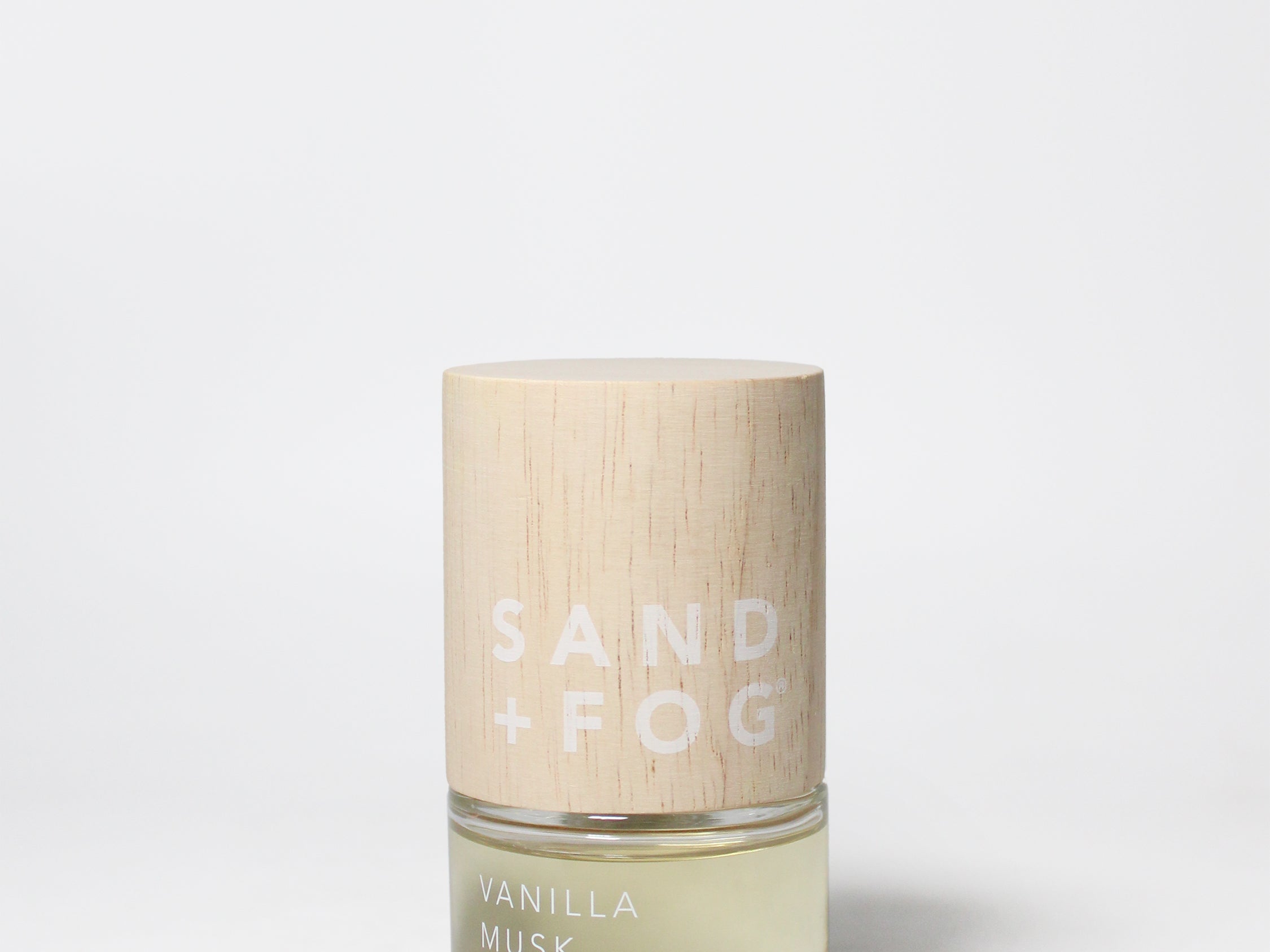 Perfume oil rollerball bottle with amber base and gold cap, labeled SAND + FOG VANILLA MUSK