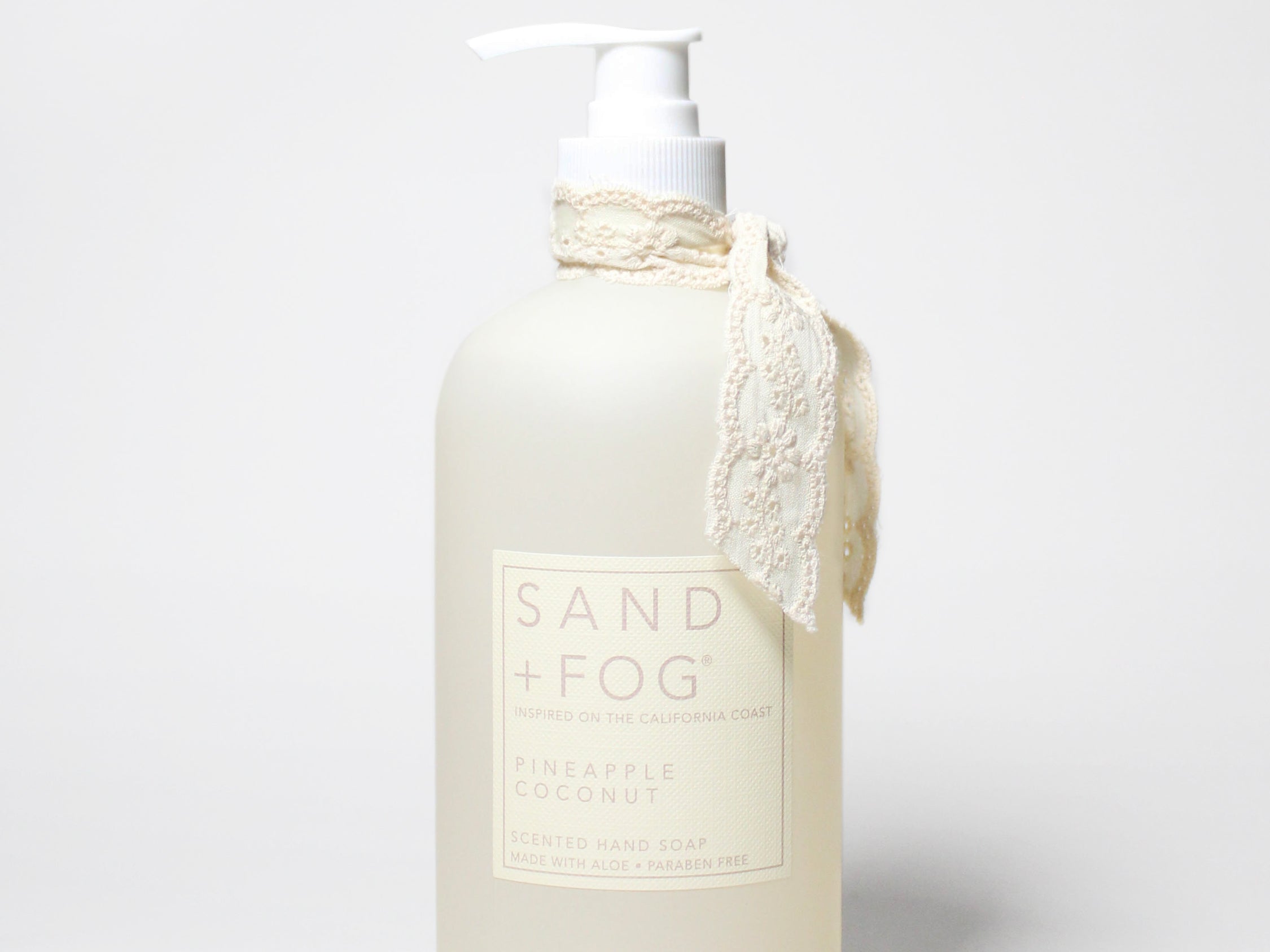 Cream liquid hand soap bottle with white pump, lace tie and 'SAND & FOG' label